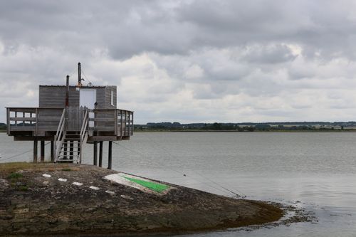 Free A scenic view of a wooden hut on stilts by a tranquil lake under a cloudy sky. Stock Photo