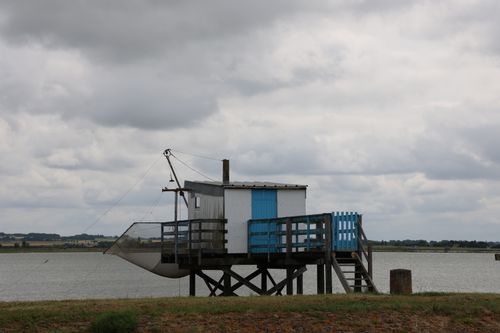 Free A solitary fishing hut on stilts overlooking a calm river on a cloudy day, evoking tranquility. Stock Photo