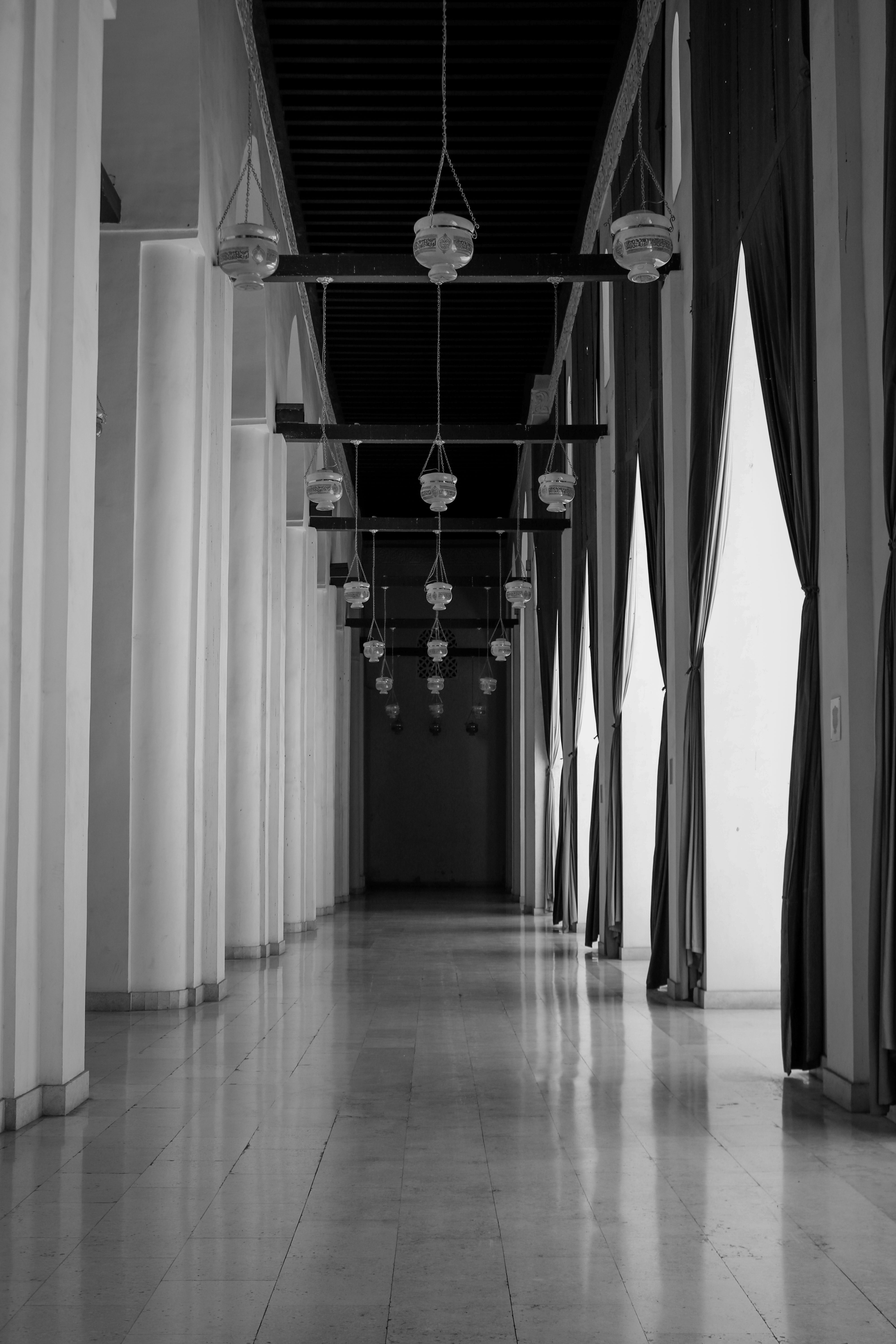 A peaceful corridor inside a historic Cairo mosque, featuring arches and hanging lamps.
