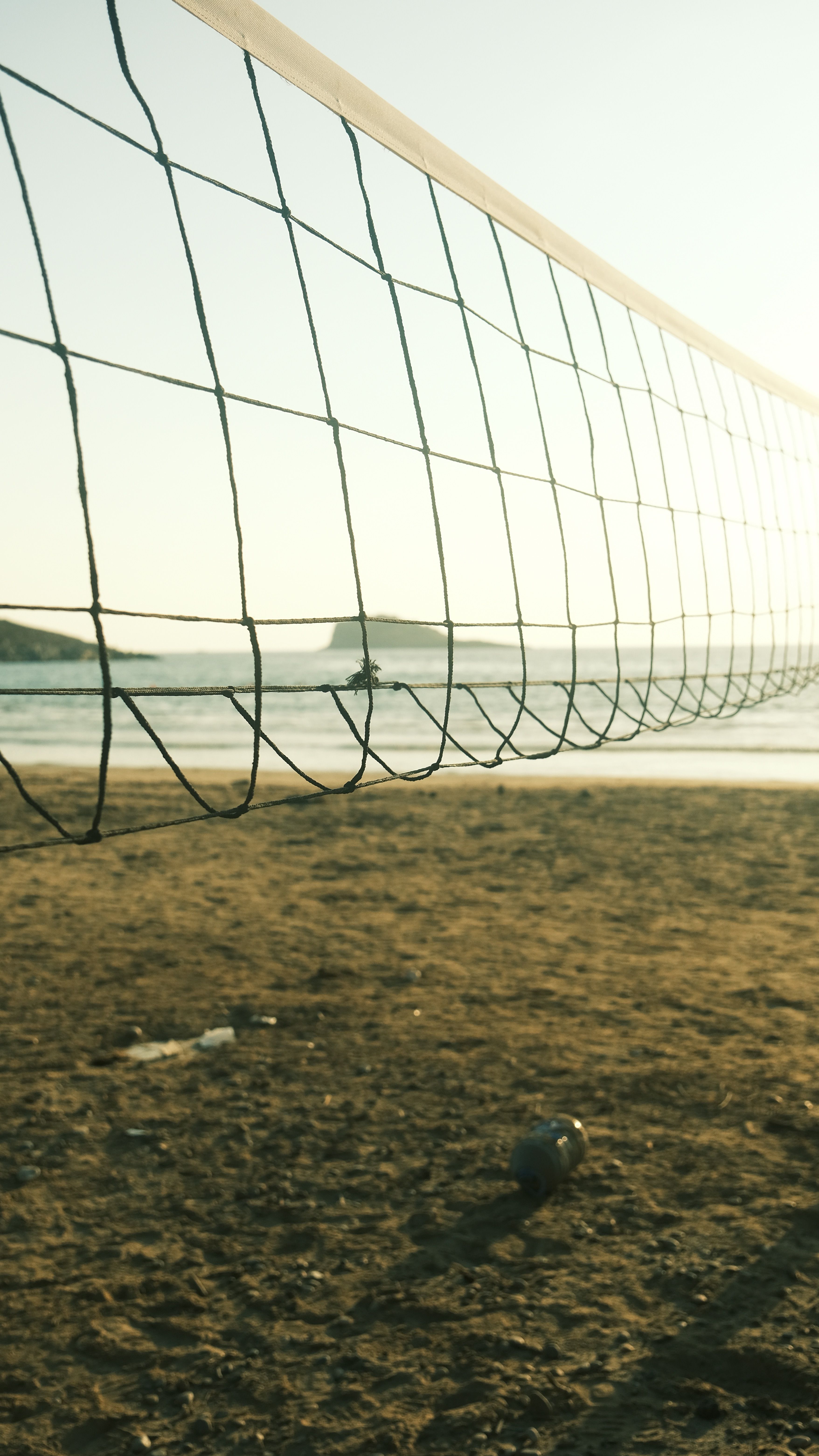 Volleyball net on a sandy beach during sunset with a serene sea background.