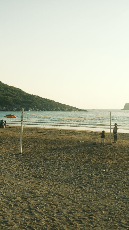 Free Children playing volleyball on a serene beach at sunset, with a hilly backdrop. Stock Photo