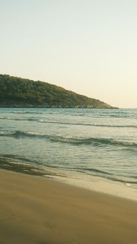 Serene beach with gentle waves and a distant hill at sunrise, offering tranquility.