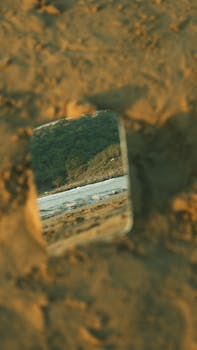 A scenic reflection of a beach landscape in a sand-surrounded mirror.