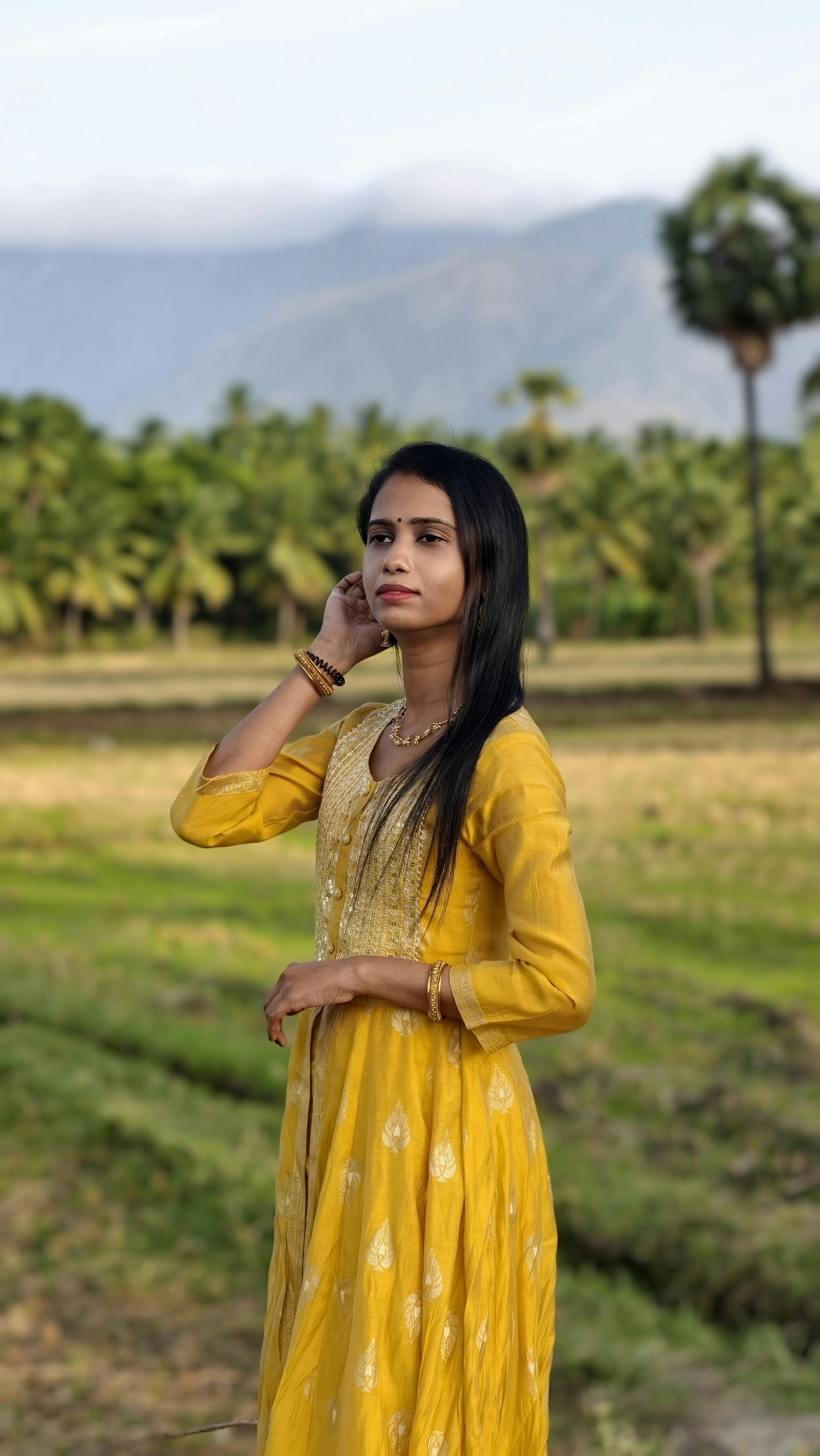 A woman in a yellow traditional outfit standing in a lush field in Tamil Nadu.