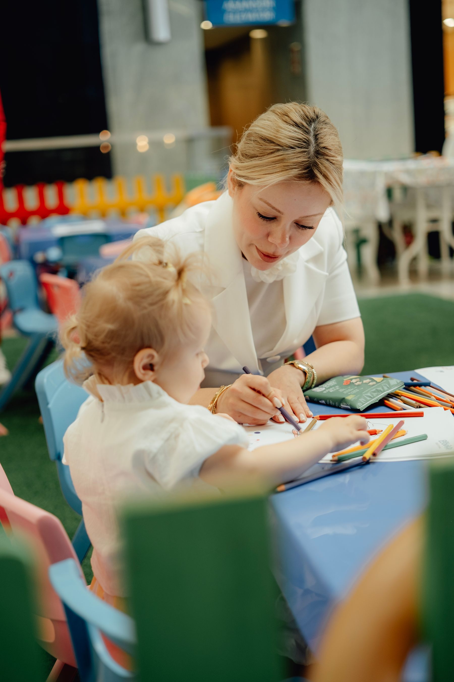 A mother guiding a young child during a colorful drawing activity with crayons at a learning table