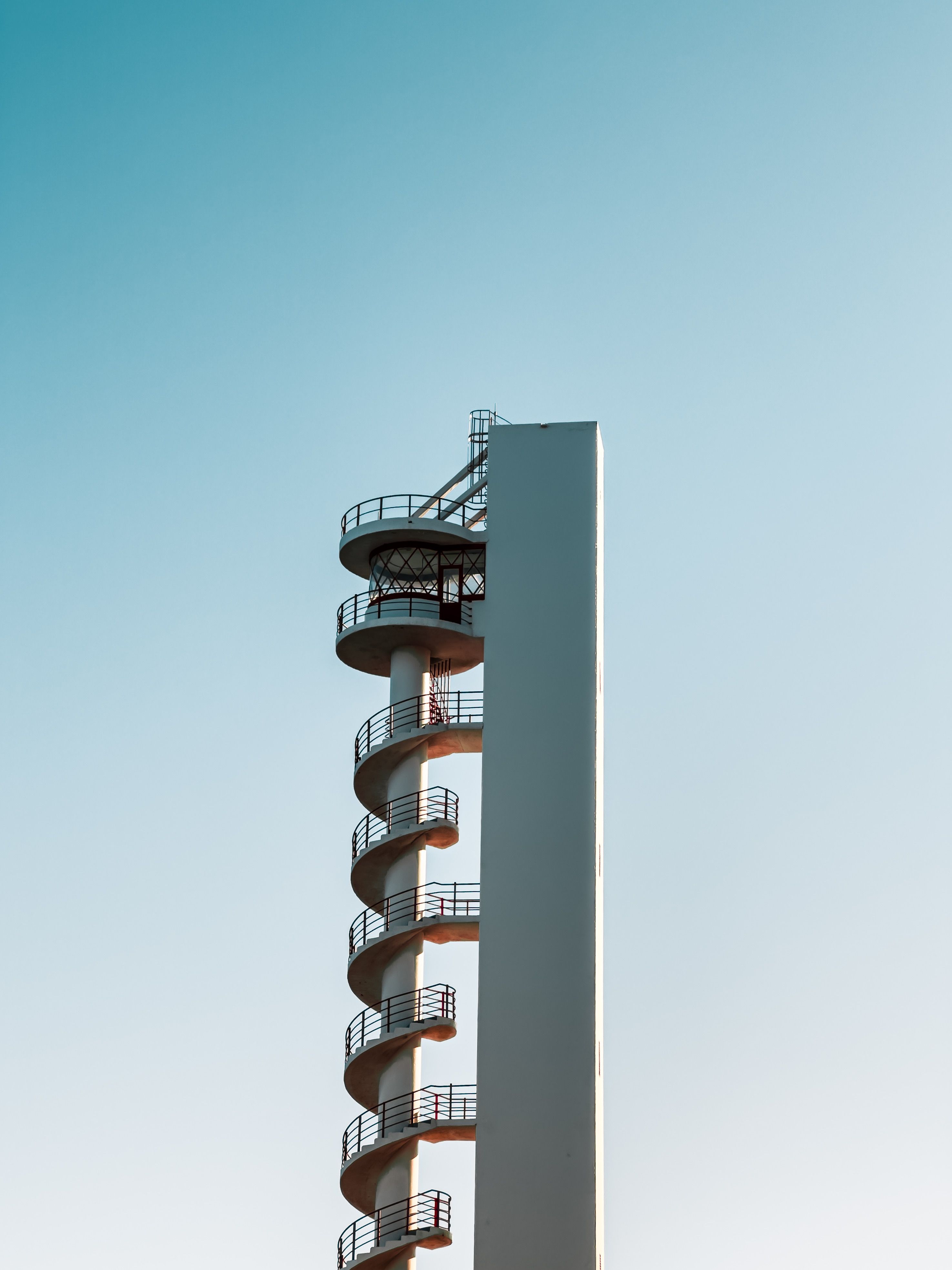 A modern spiral stair tower with minimalistic design against a clear blue sky, located in España.