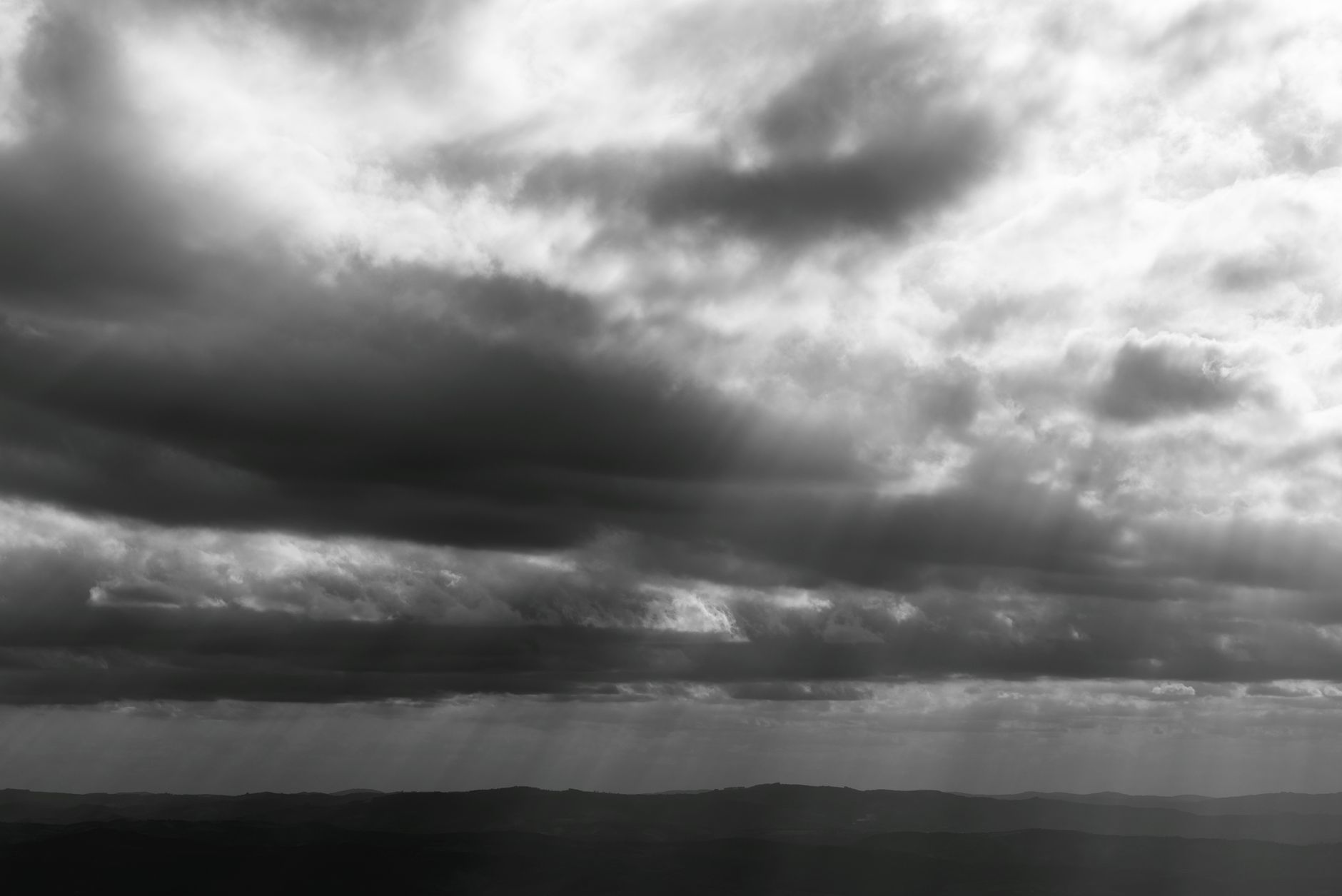 Black and white dramatic sky with sun rays over Minas Gerais hills.