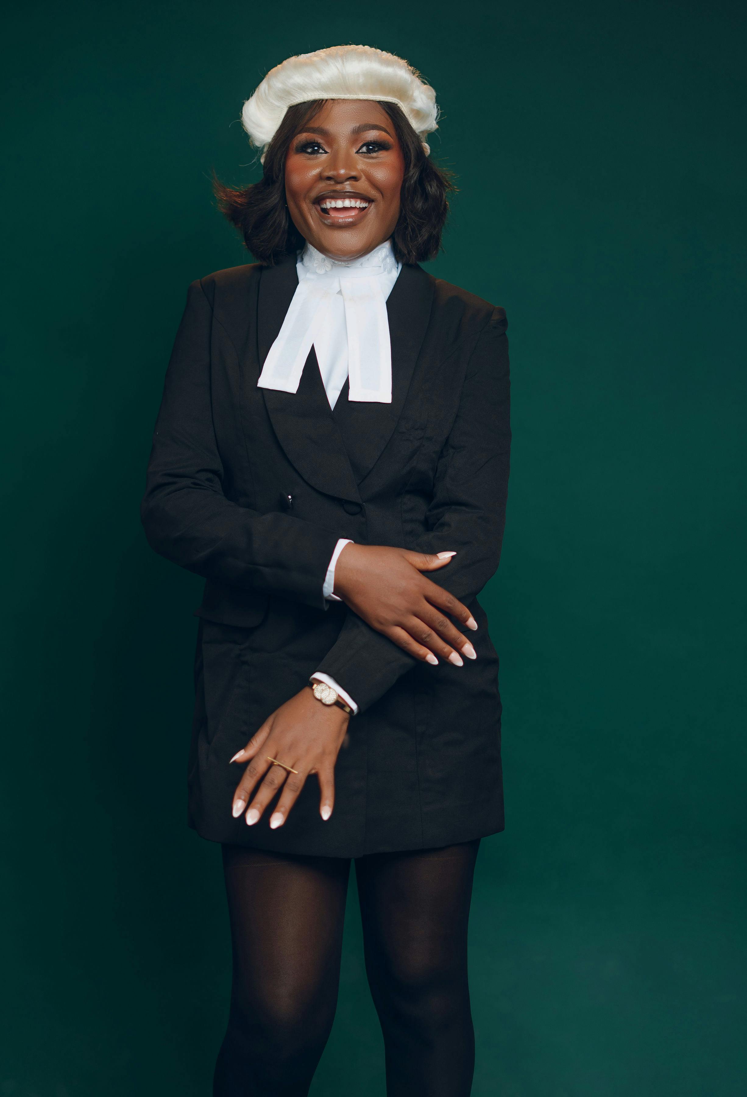 Smiling female lawyer posing confidently in traditional legal attire against a green background.