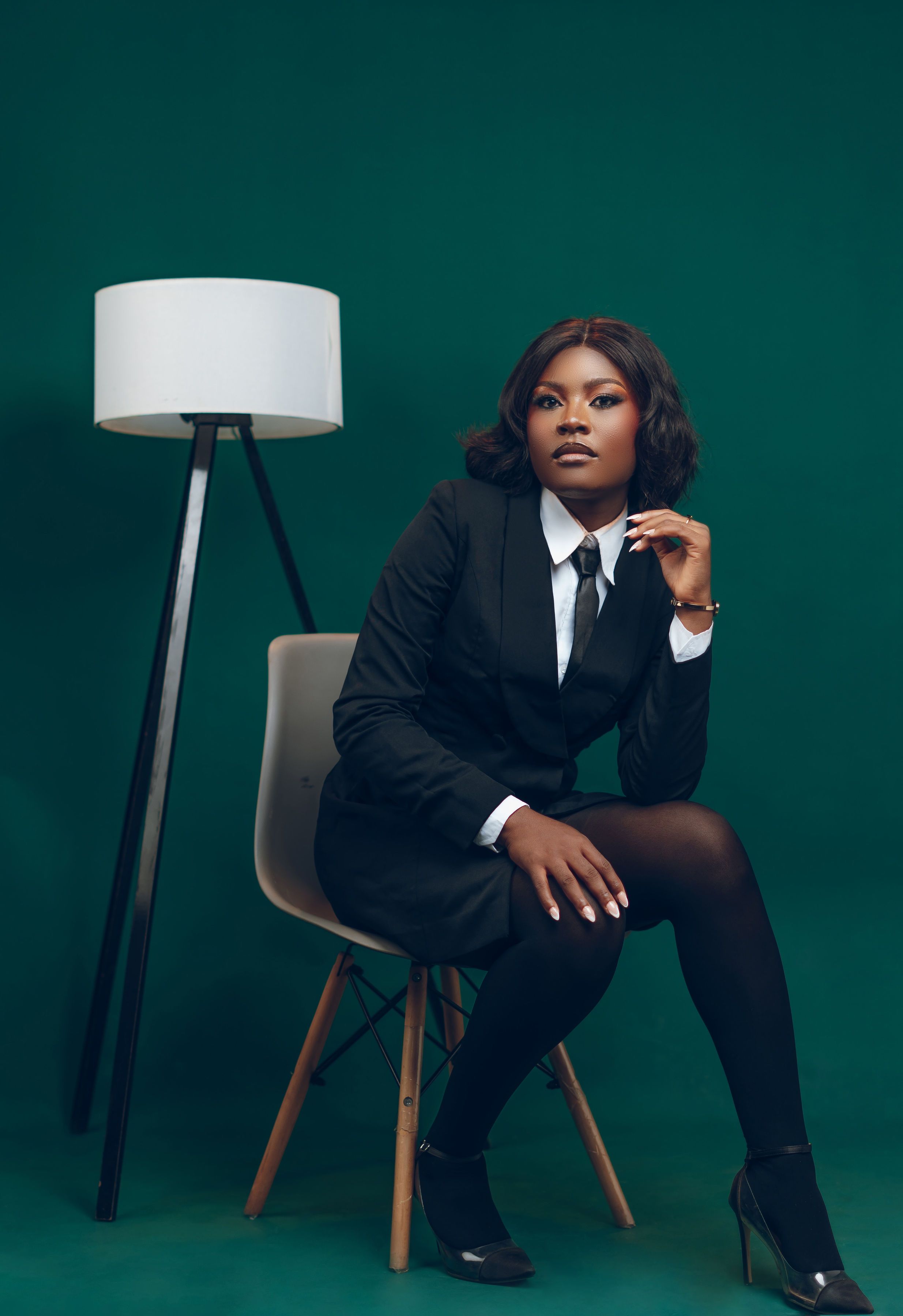 Confident woman in business attire sitting beside a modern lamp.