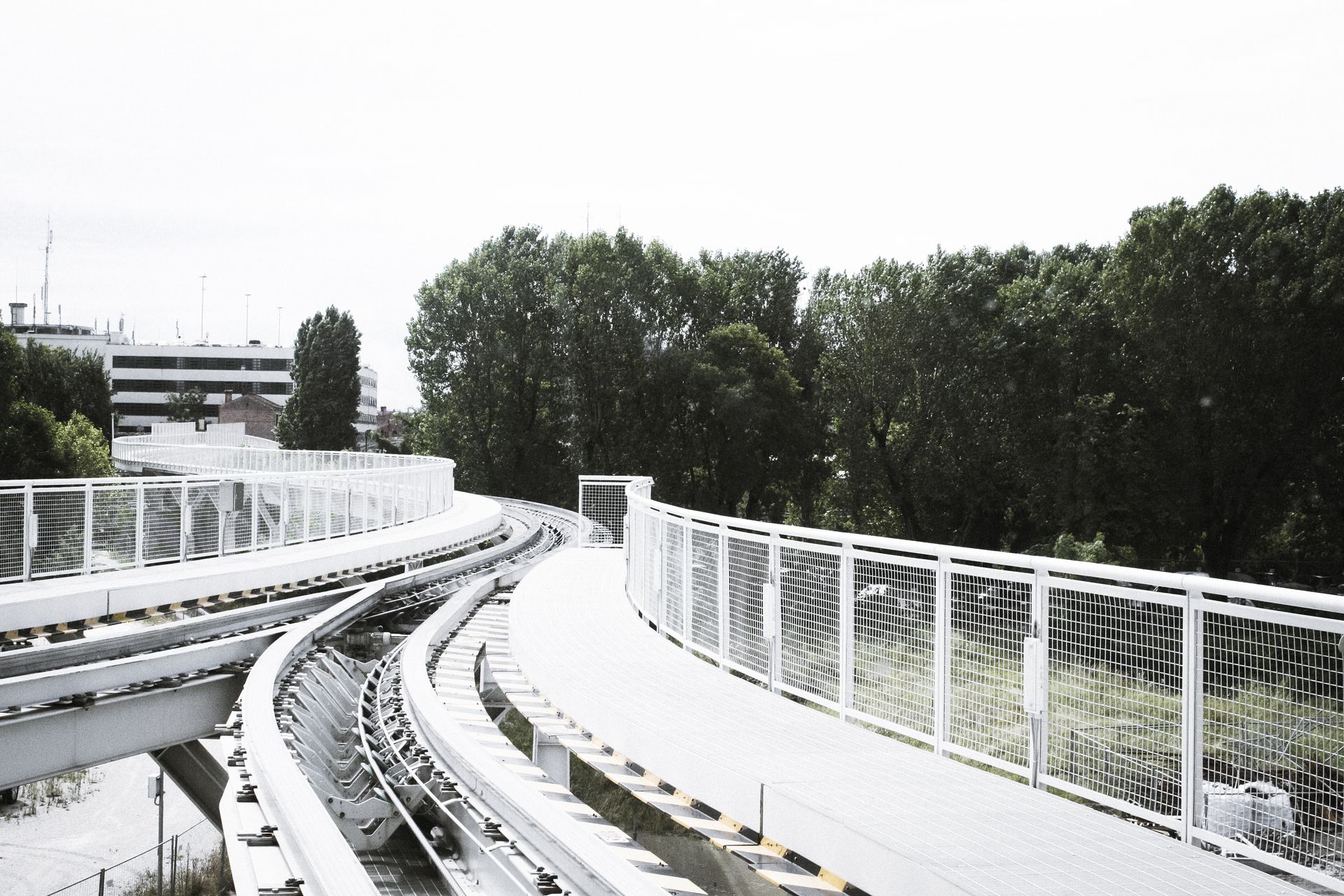 Curved railroad tracks with modern railings in an urban area surrounded by trees and buildings.