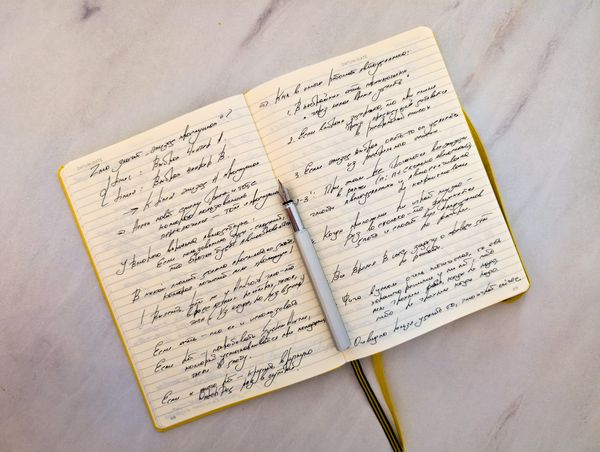 Open notebook of cursive handwriting with a pen resting on the page — Max Grakov on Pexels
