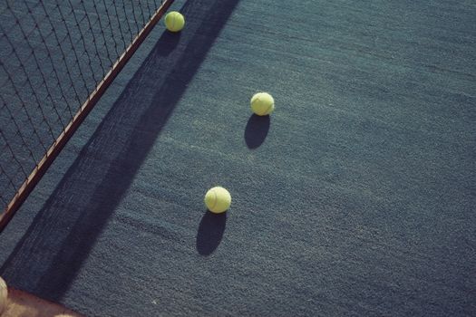 Tennis balls scattered on a sunlit tennis court, casting shadows.