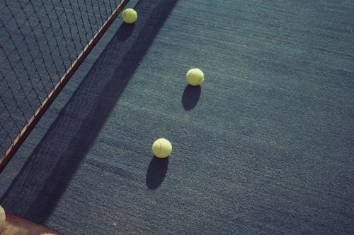 Free Tennis balls scattered on a sunlit tennis court, casting shadows. Stock Photo