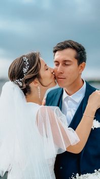 Bride kisses groom on a cloudy day, celebrating love and commitment.