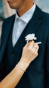 Close-up of elegant wedding suit with white boutonniere being adjusted.