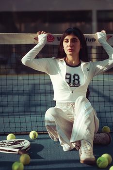 Woman in sportswear sitting on a tennis court, surrounded by tennis balls and paddle.