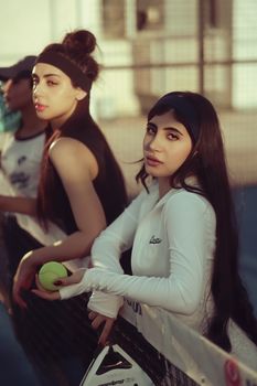 Two young women leaning on a tennis net during a sunny day in Baghdad, Iraq.