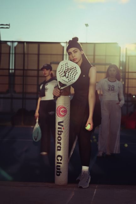Dynamic shot of three women enjoying padel tennis at sunset in an outdoor court.