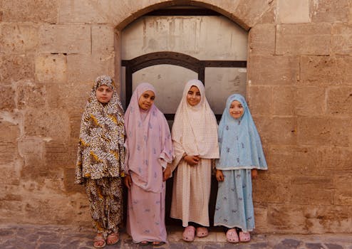 Four children wearing colorful hijabs smiling in front of a stone wall in Şanlıurfa, Türkiye.