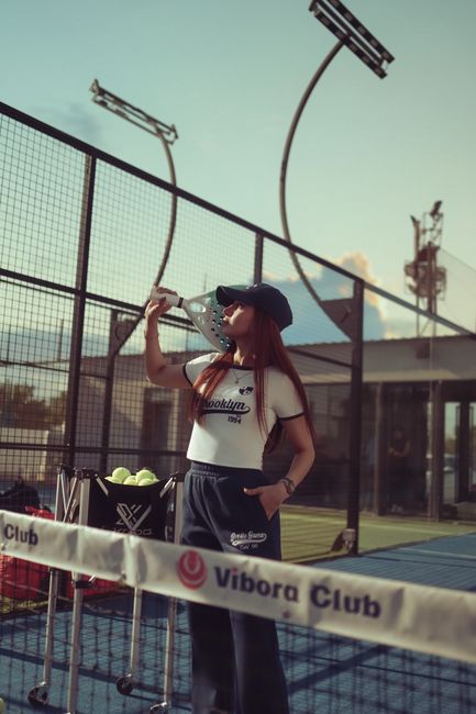 Young woman hydrating on an outdoor padel court under a clear sky.