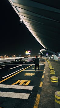 Lone figure stands under modern architecture at Beijing International Airport at night.