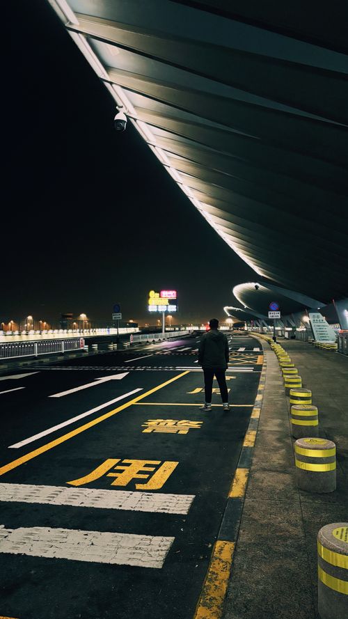 Free Lone figure stands under modern architecture at Beijing International Airport at night. Stock Photo
