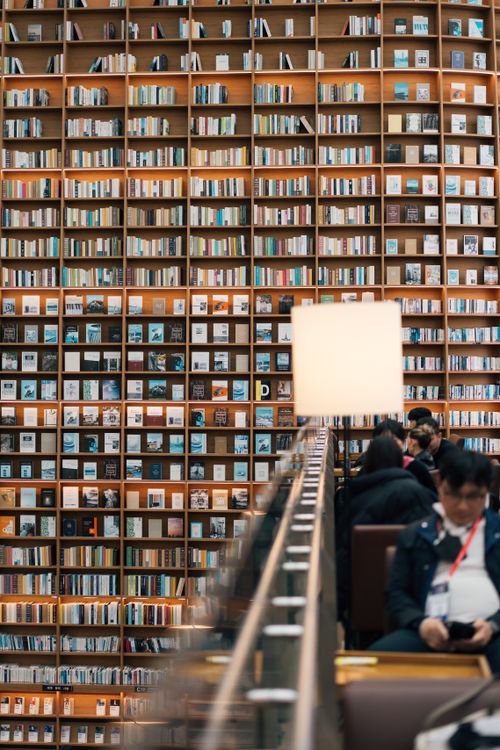 Free Expansive modern library featuring towering book walls and seated visitors. Stock Photo