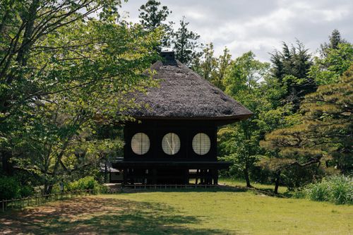 Free A serene traditional Japanese thatched house surrounded by lush greenery. Stock Photo