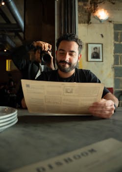 A man reading a menu at a trendy cafe in London, with a photographer capturing the moment in a cozy setting.