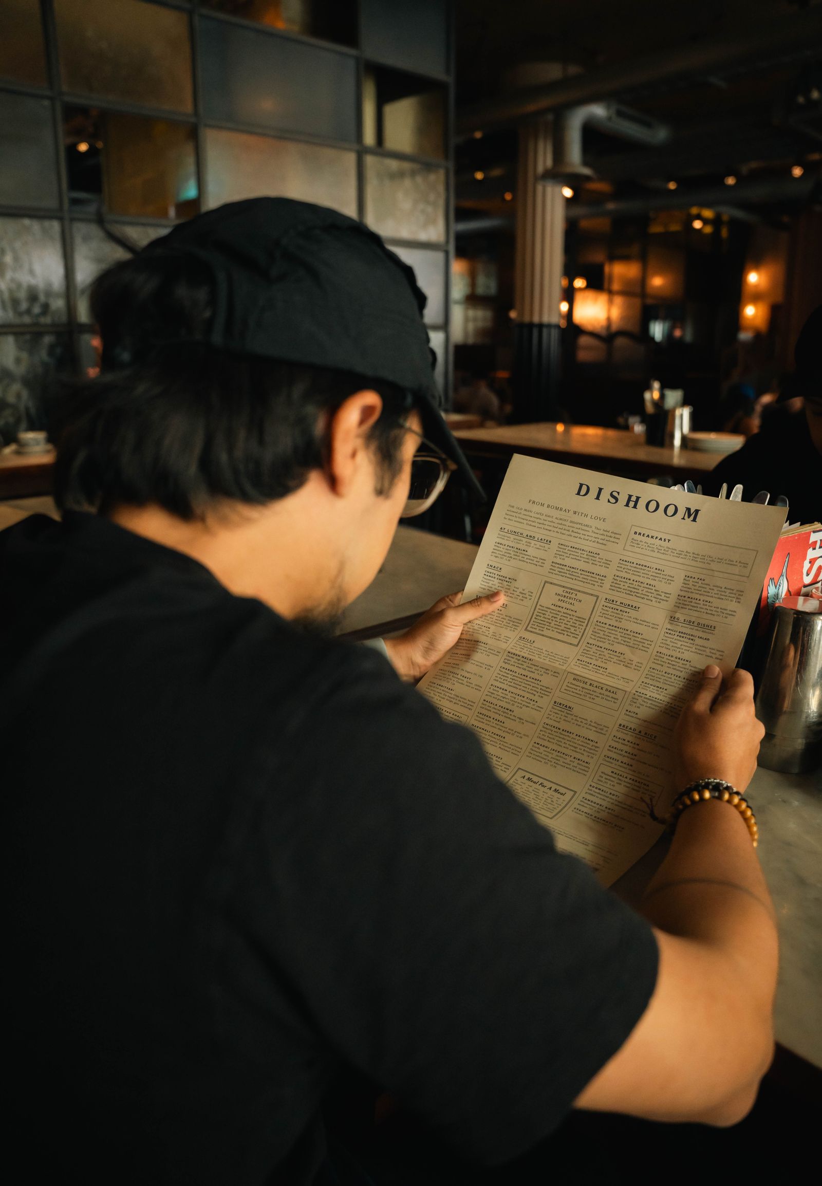 A guest reading the menu inside Dishoom's warm, Bombay cafe styled dining room