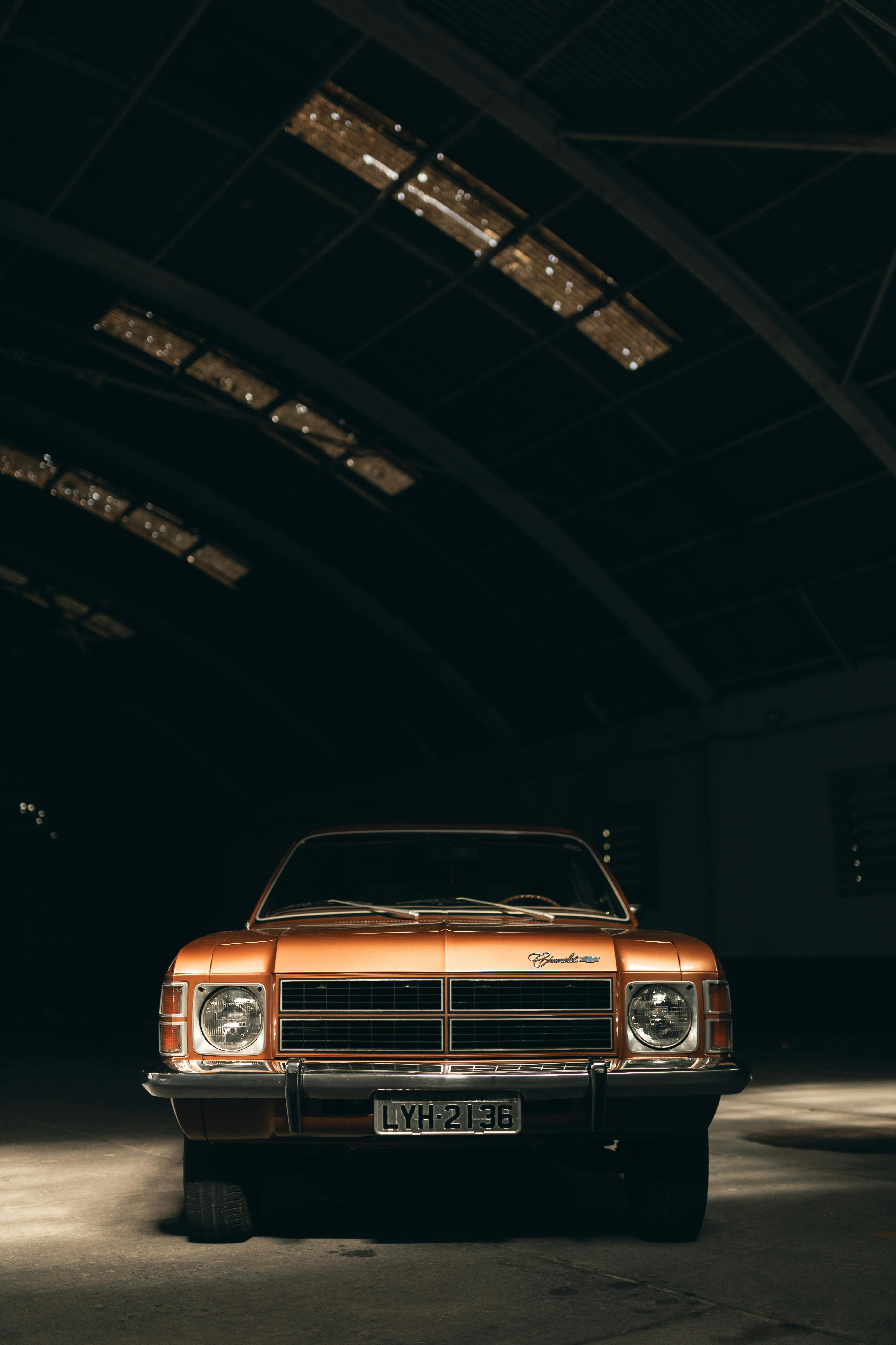 Front view of a classic orange car in a dimly lit warehouse.