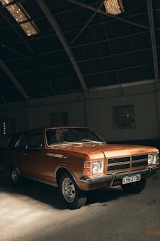 Classic orange car parked in an industrial looking warehouse under soft lighting.