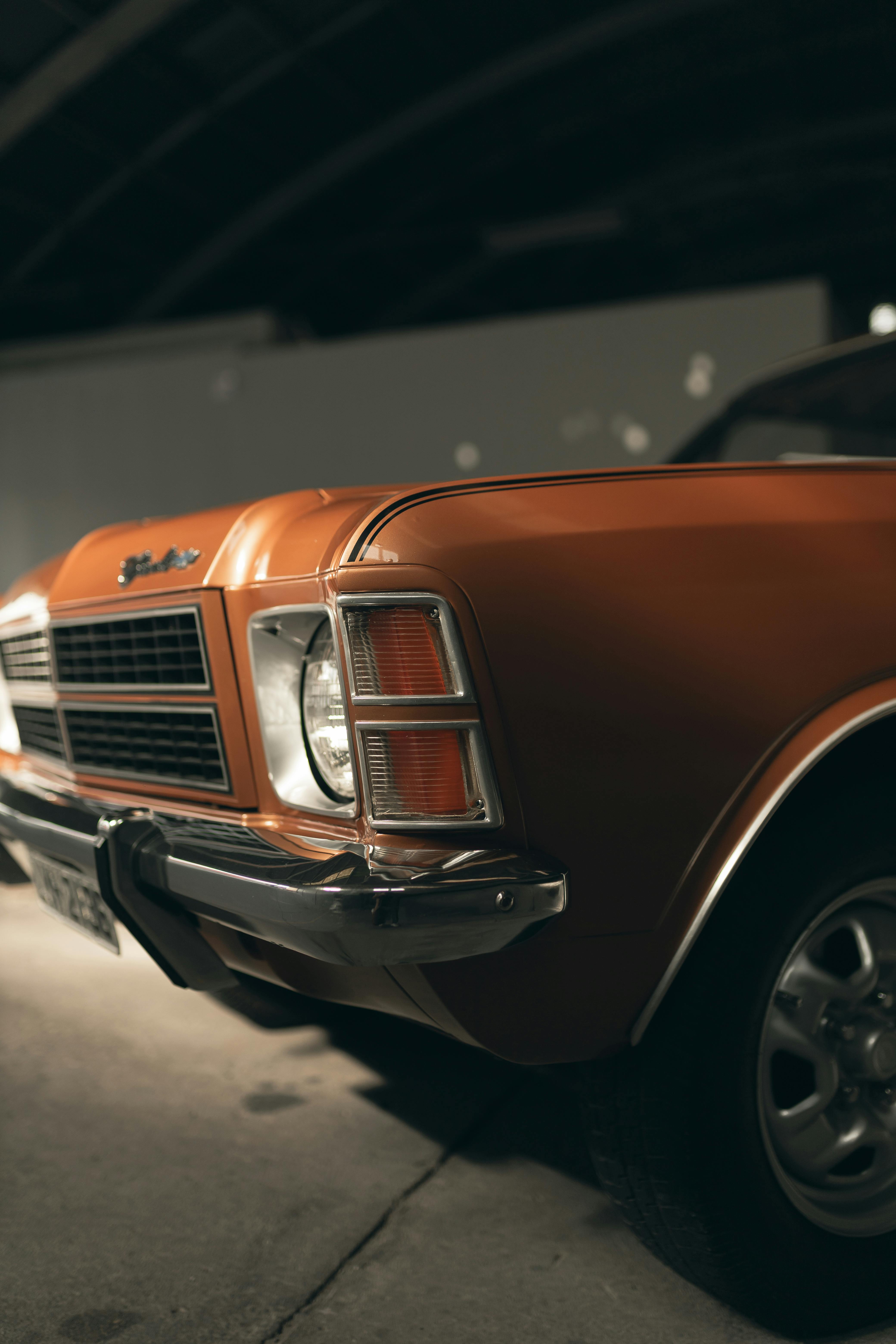 Close-up of a vintage orange car's front in a dimly lit garage. Classic automotive elegance.