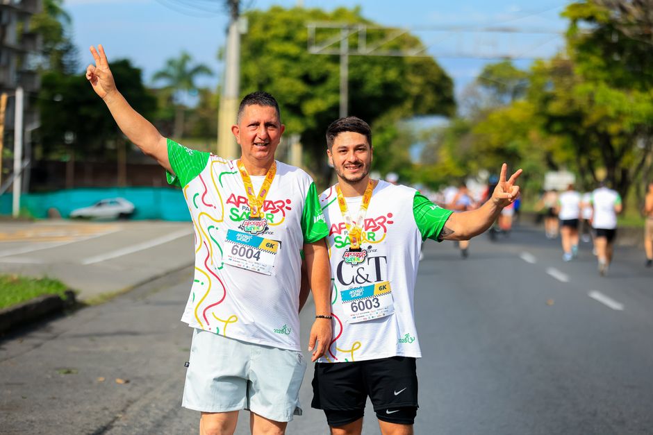Two men proudly pose after completing a marathon, showing peace signs and medals.