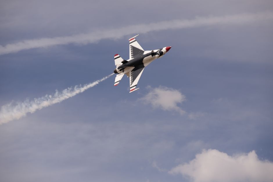 Jet fighter flying at high speed with vapor trails against a blue sky.