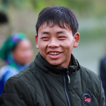 Portrait of a smiling young man in Lào Cai, Vietnam, wearing traditional Hmong attire.