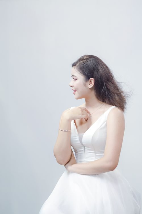 Free Graceful profile portrait of a woman in a stylish white dress against a soft light background. Stock Photo