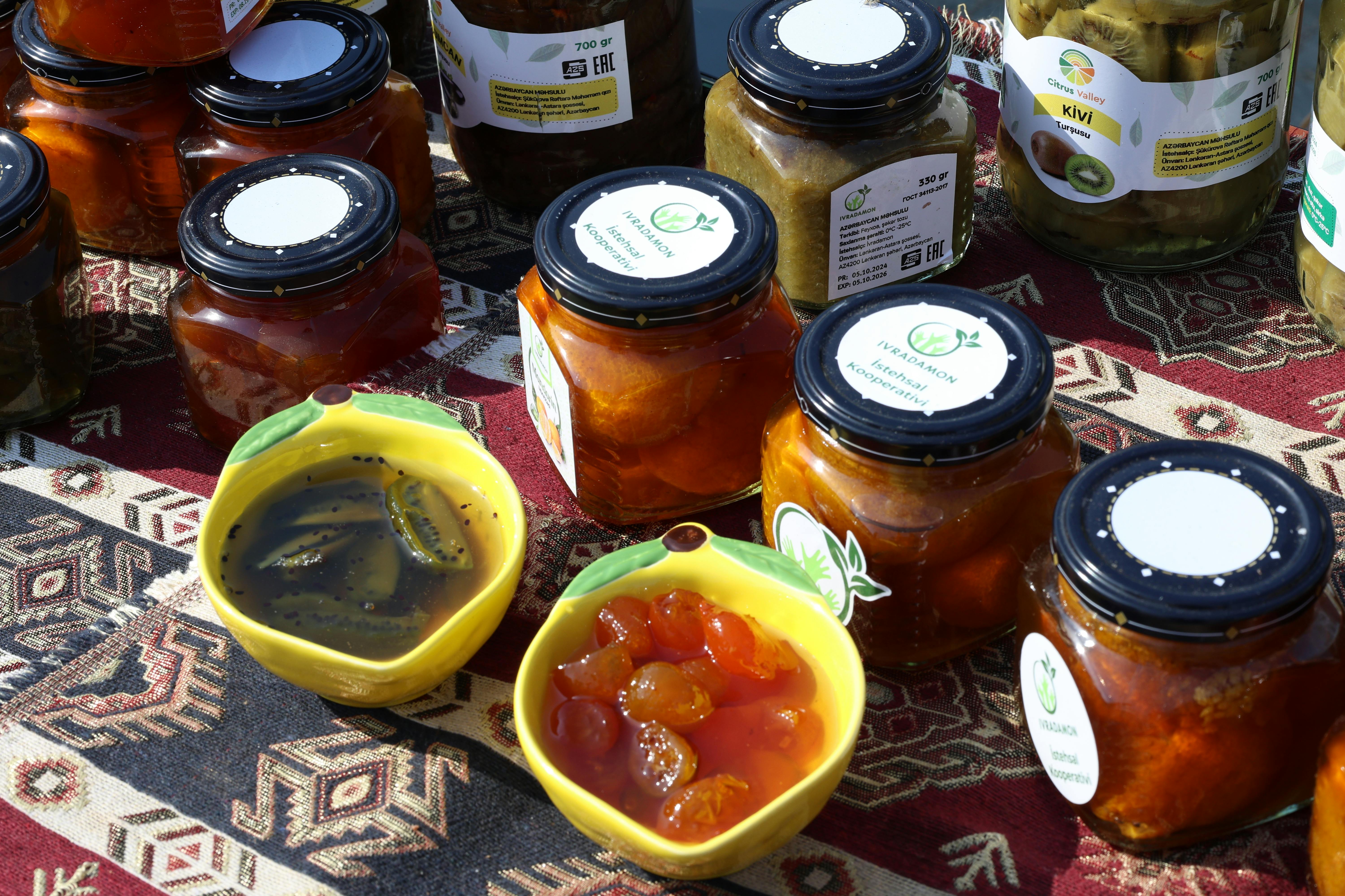 Colorful jars of homemade preserves and jams on a traditional patterned cloth.