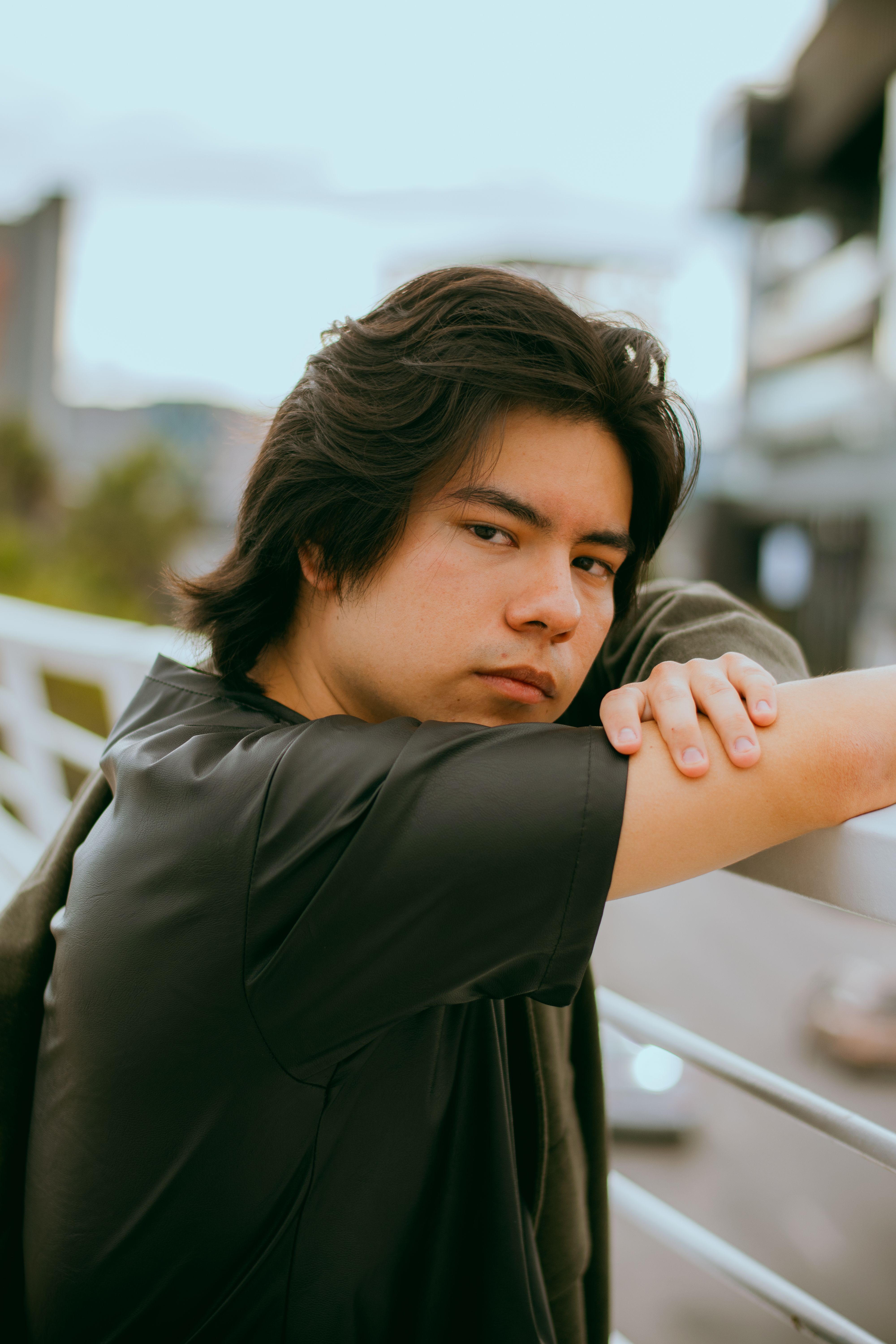 Close-up of a young adult man leaning on a railing with a pensive look.