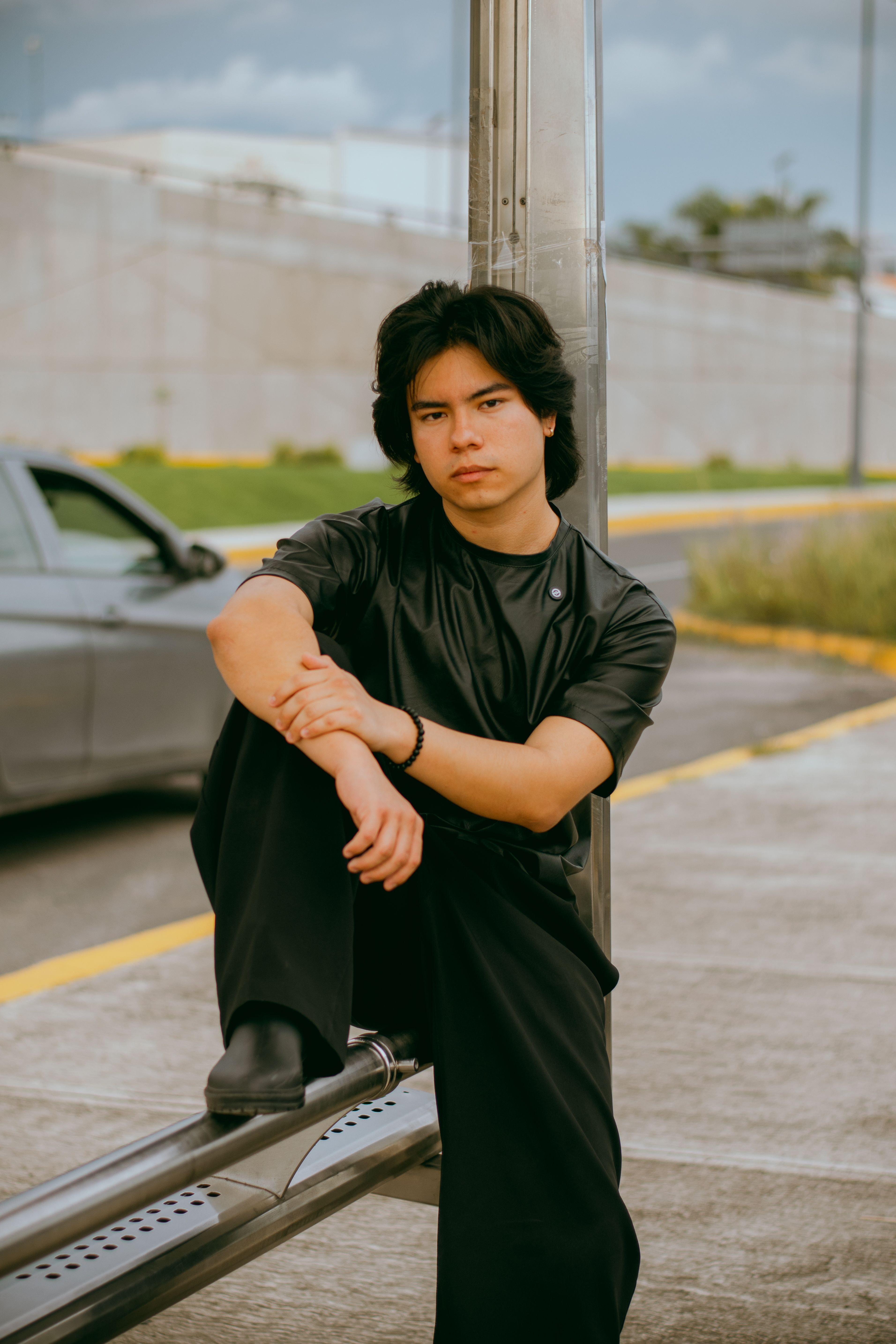 Young man sitting thoughtfully by roadside in urban setting. Casual, reflective moment.