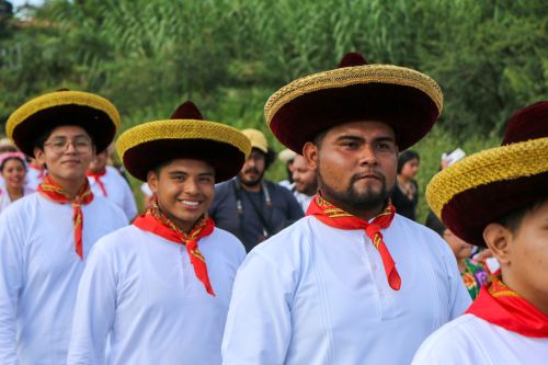 Free Men in traditional attire with hats participate in a colorful cultural parade outdoors. Stock Photo