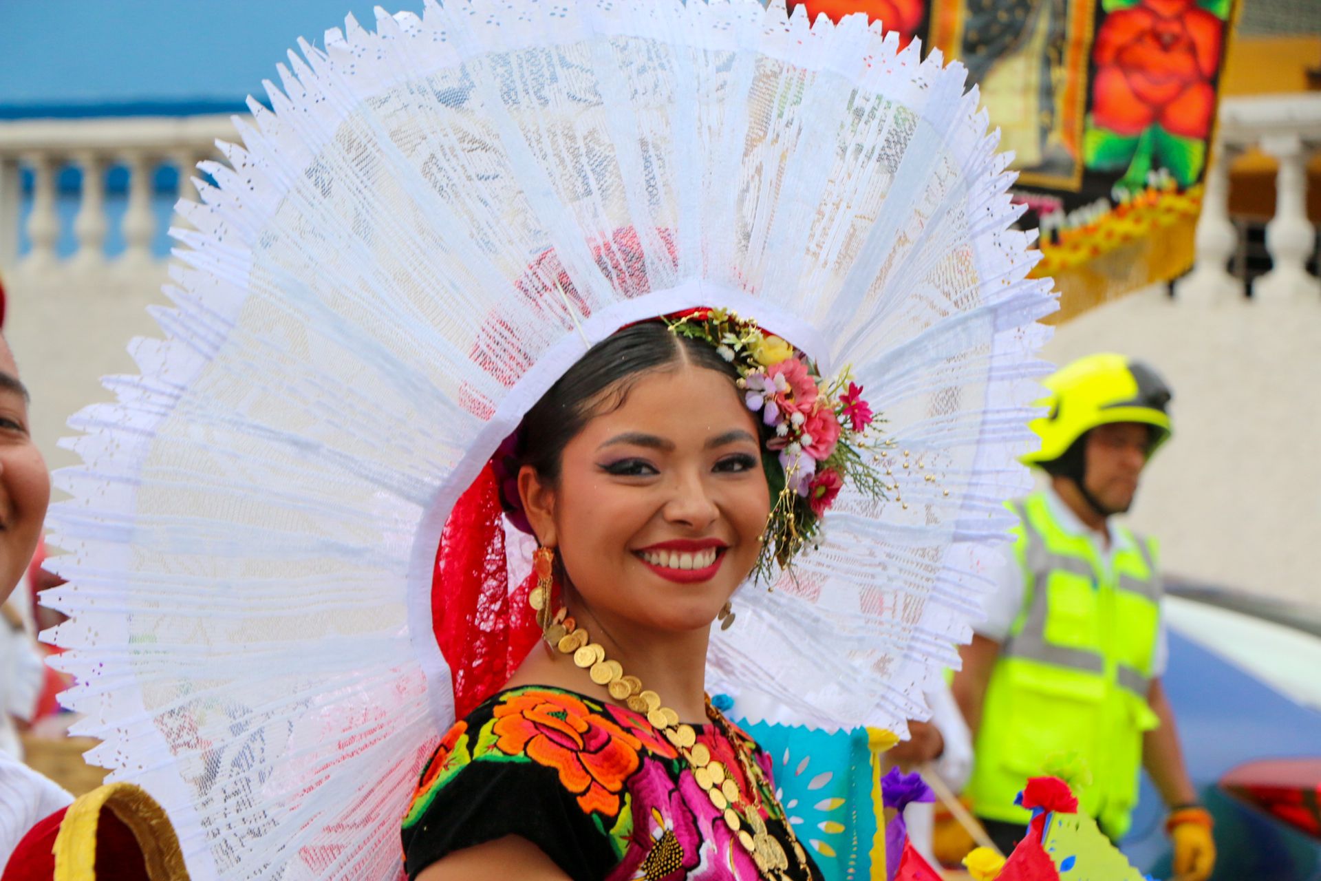 A woman in colorful traditional Mexican attire smiling during a festival parade.