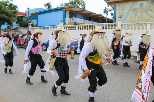 Group of dancers in traditional attire with masks and hats at cultural festival outdoors.