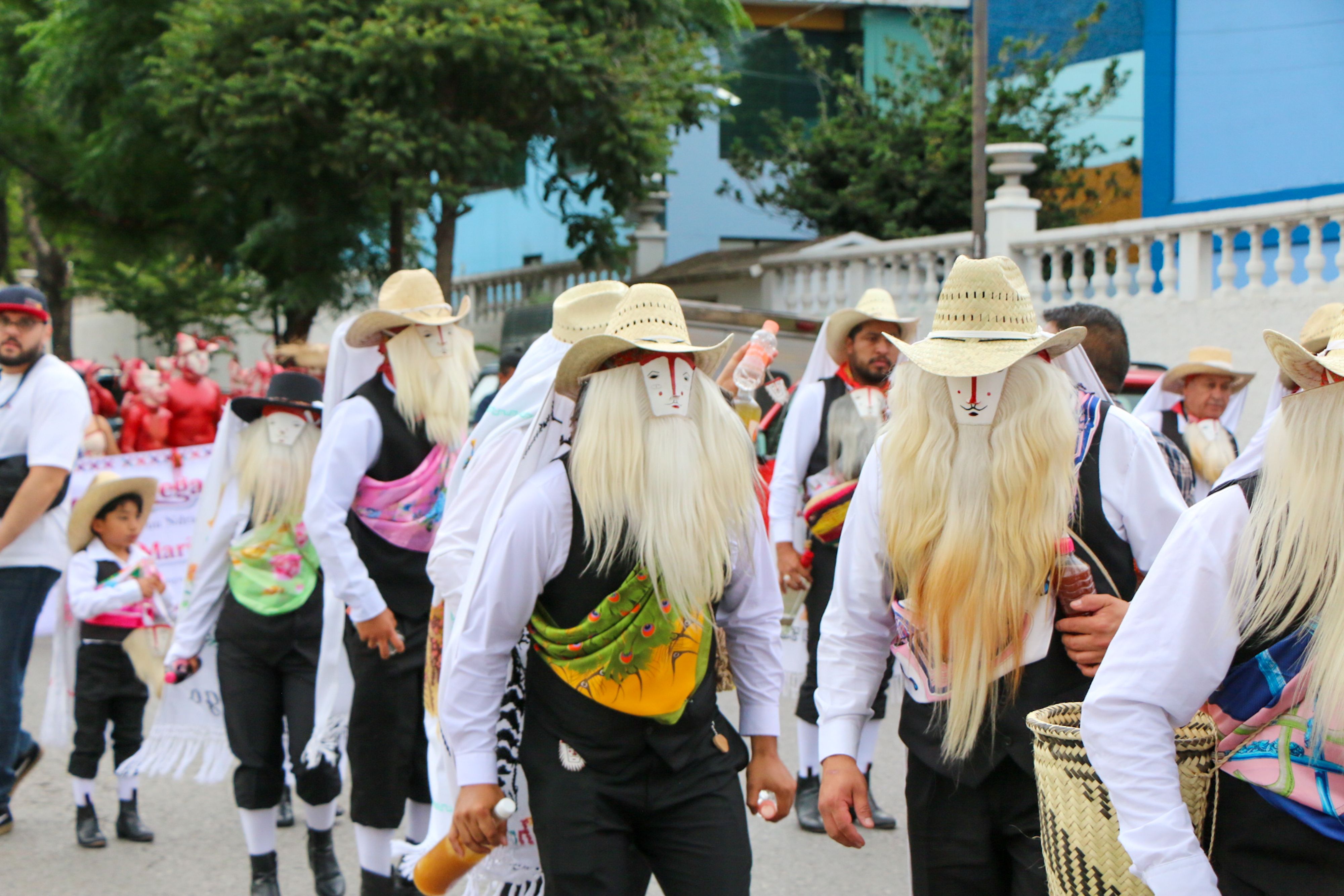 Colorful Mexican cultural parade with dancers in traditional costumes and masks during daylight.