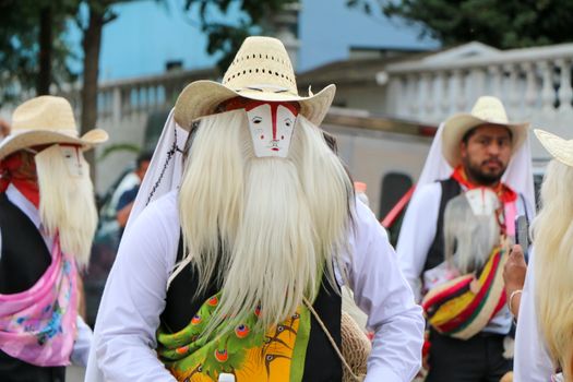 Masked dancers in traditional attire participate in a vibrant cultural festival outdoors.