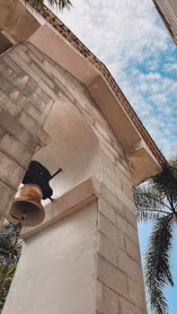 A low-angle shot of a bell tower with a clear blue sky and palm fronds.