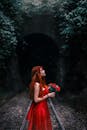 一位身着红色连衣裙的优雅女子，捧着鲜花，在黑暗的隧道旁摆姿势