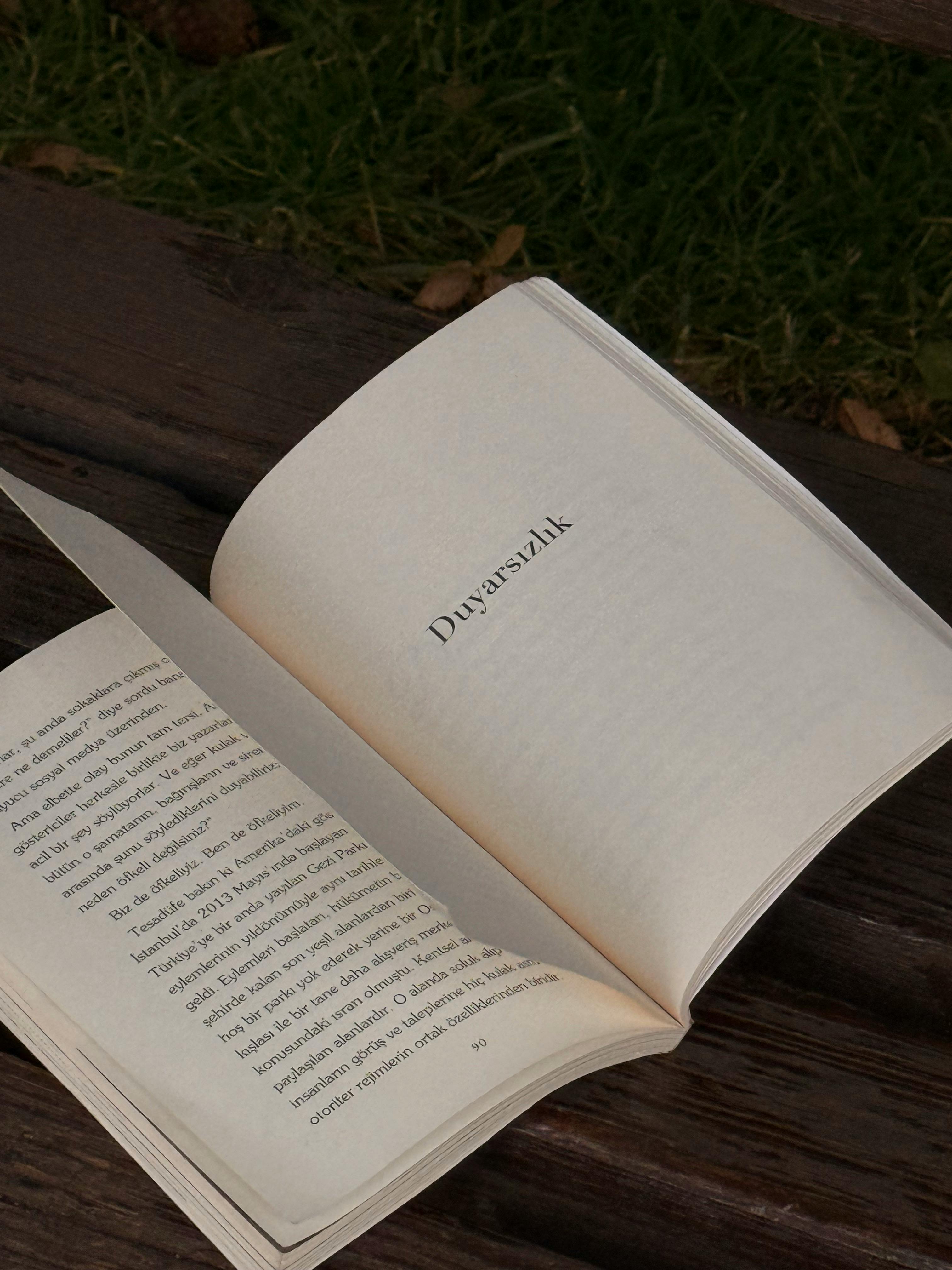 An open book on a wooden bench in an outdoor setting, pages turning.