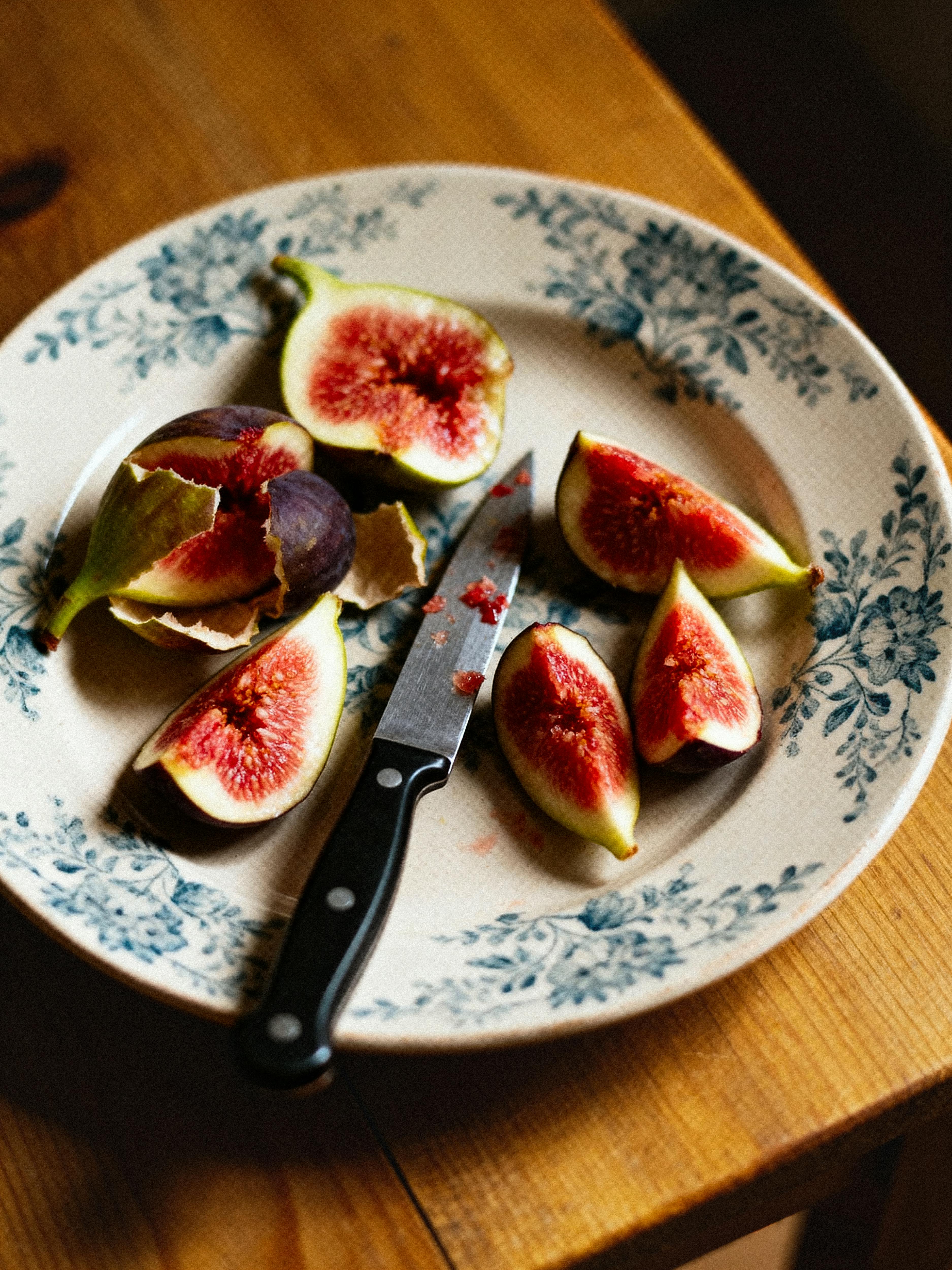 Sliced fresh figs on a decorative plate with a knife on a wooden table.