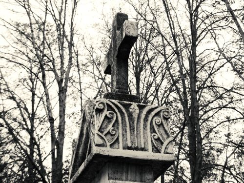 Free A vintage black and white image of a stone cross monument set against bare trees, conveying nostalgia. Stock Photo